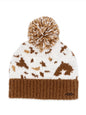 Ivy's Gifts & Boutique cow print beanie with fluffy ball top, cozy knit hat featuring black and white cow pattern and pom-pom on top.