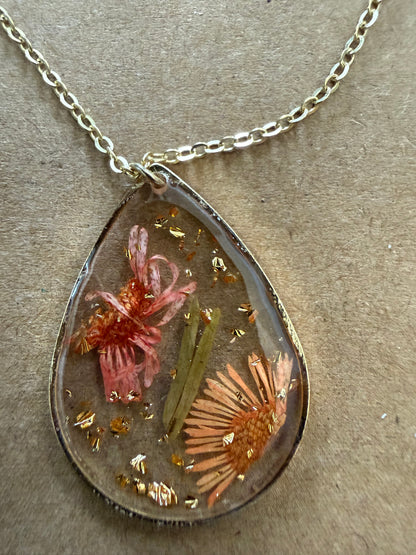 Dried flower pendant necklace with clear glass globe, featuring preserved blooms on a silver chain, by Ivy's Gifts & Boutique.