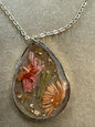 Dried flower pendant necklace with clear glass globe, featuring preserved blooms on a silver chain, by Ivy's Gifts & Boutique.