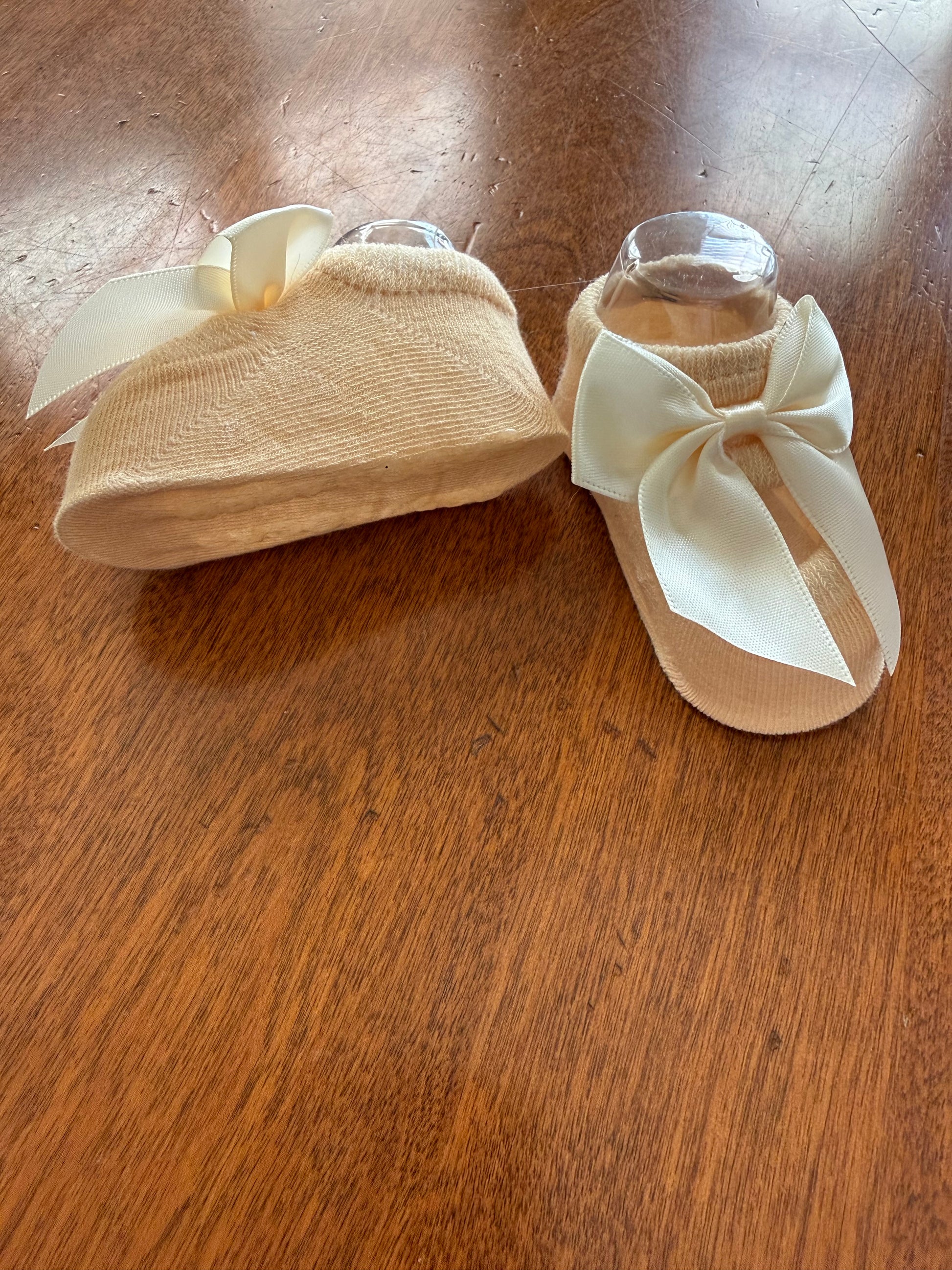 Baby infant booties from Ivy's Gifts & Boutique with ivory bow, soft fabric and cozy fit for little feet.