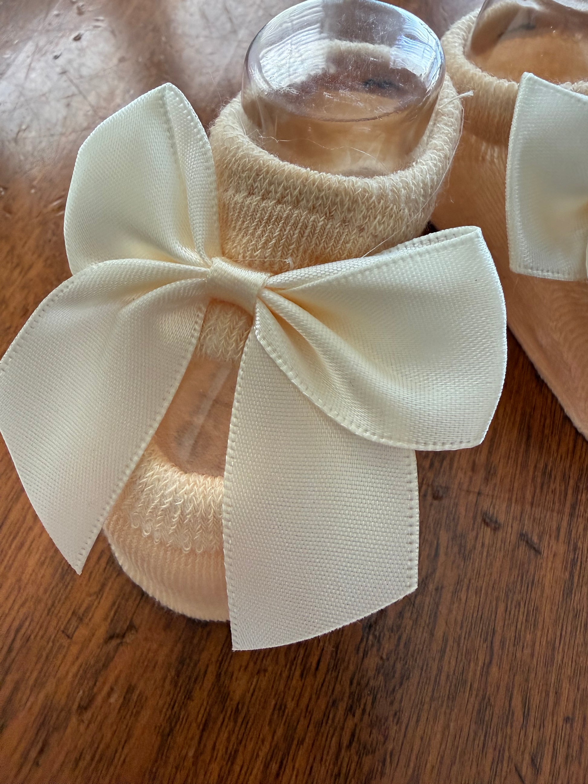 Ivory baby booties with a bow from Ivy's Gifts & Boutique, soft infant footwear for newborns and babies.