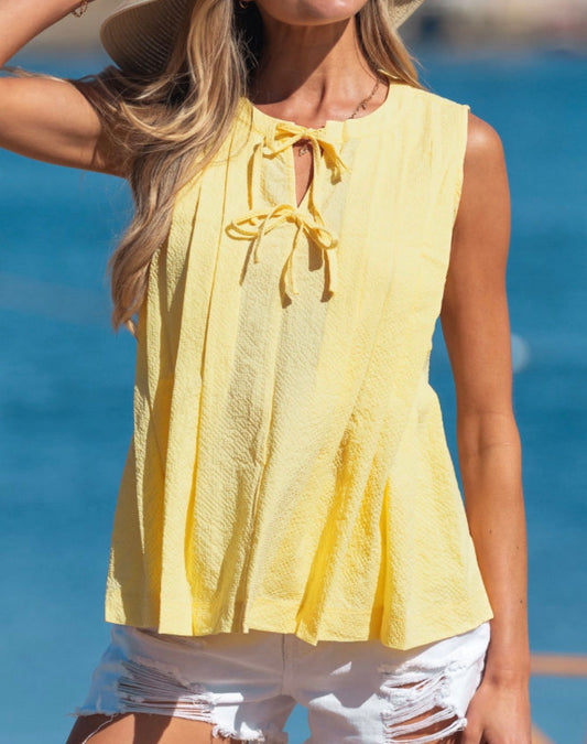 Yellow sleeveless blouse by Ivy's Gifts & Boutique with trendy bow closure and pleated design, shown on a model.