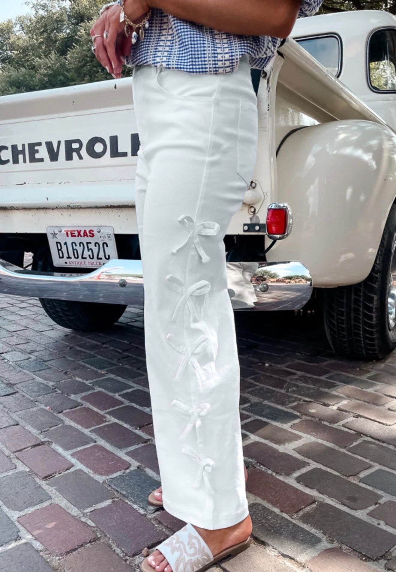 White jeans by Ivy's Gifts & Boutique featuring side seam bow details and a slim fit, displayed on a model.
