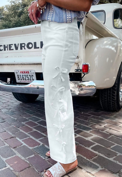 White jeans by Ivy's Gifts & Boutique featuring side seam bow details and a slim fit, displayed on a model.