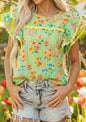 Green summer floral print top by Ivy's Gifts & Boutique with ruffled cap sleeves and ric rac trim, shown on a hanger.